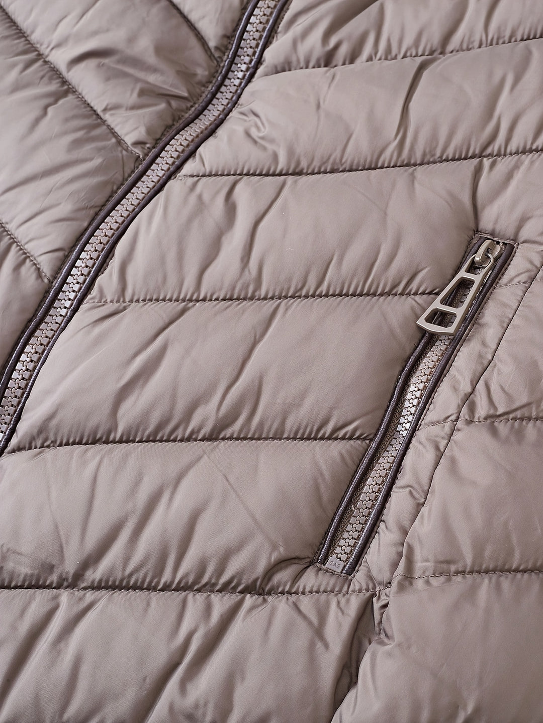 Taupe quilted winter coat fabric detail with visible zipper and seam stitching.