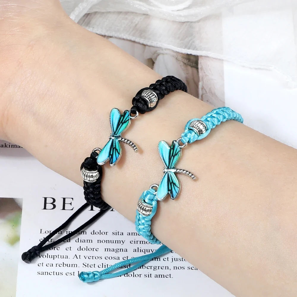 Set of two handwoven bracelets on wrists: black and light blue cords with dragonfly charms
