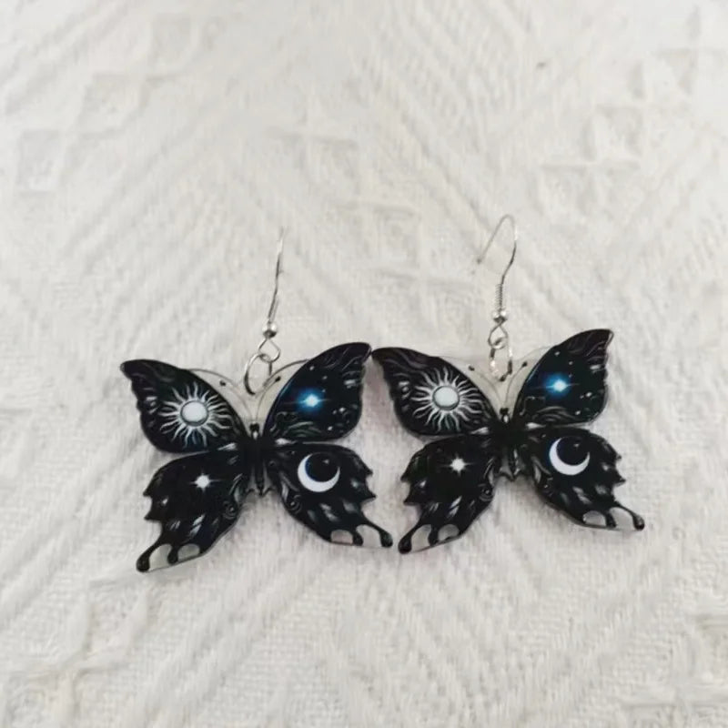 Pair of black butterfly dangle earrings with moon and star details, silver hooks.